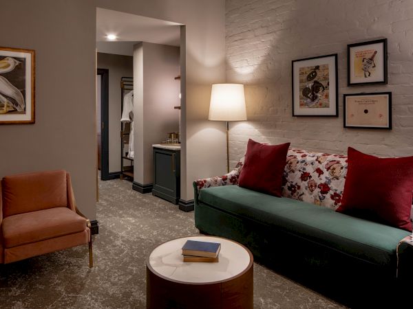 A cozy living room with a floral sofa, red pillows, a round coffee table, a side chair, floor lamp, and framed art on neutral walls.