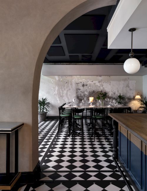 A stylish dining area with a black-and-white checkered floor, arched doorway, wood accents, and warm pendant lighting, creating a chic vintage vibe.