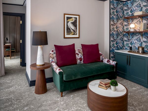 A stylish living area with a green velvet sofa, floral cushions, a round coffee table, lamp, art above, and a built-in cabinet with shelves.