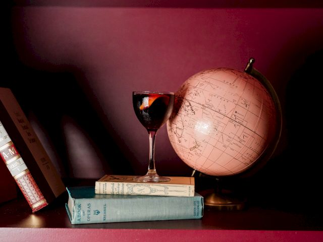 A small candle and a globe sit on a book, with a light source casting a warm glow on a red table.