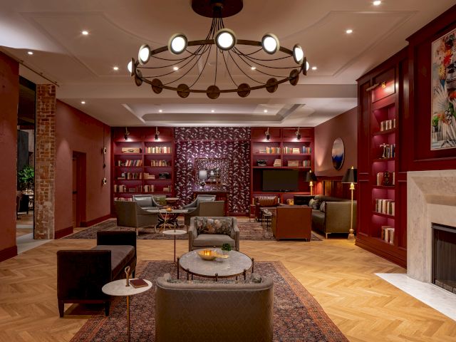 A cozy, ornate dining room with a long wooden table, warm lighting, red walls, and elegant china and floral decor.