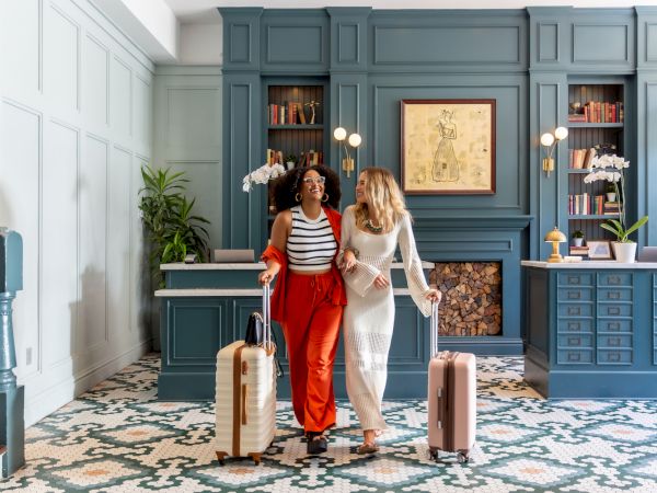 Two people with suitcases walk in a stylish lobby, featuring blue shelves and patterned flooring.