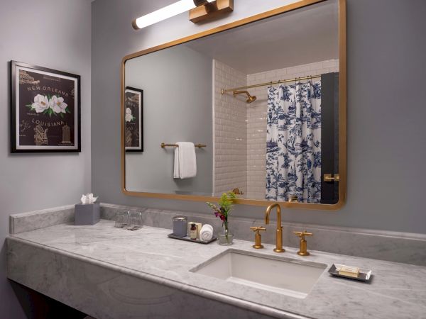 A chic bathroom vanity with a marble countertop, gold faucet, large framed mirror, and a floral shower curtain in a neutral-toned room.