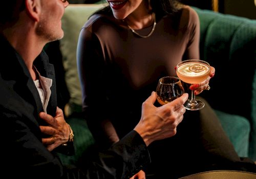 Two people clinking cocktails and chatting warmly in a cozy lounge, a stylish date vibe tonight.