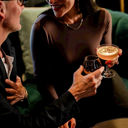 Two people clinking cocktails and chatting warmly in a cozy lounge, a stylish date vibe tonight.