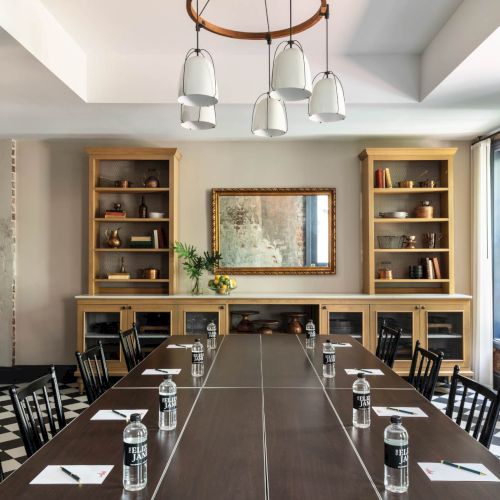 A stylish conference room with a long table, black chairs, water glasses, notepads, and a built-in shelving unit flanking a central framed mirror; industrial yet warm.
