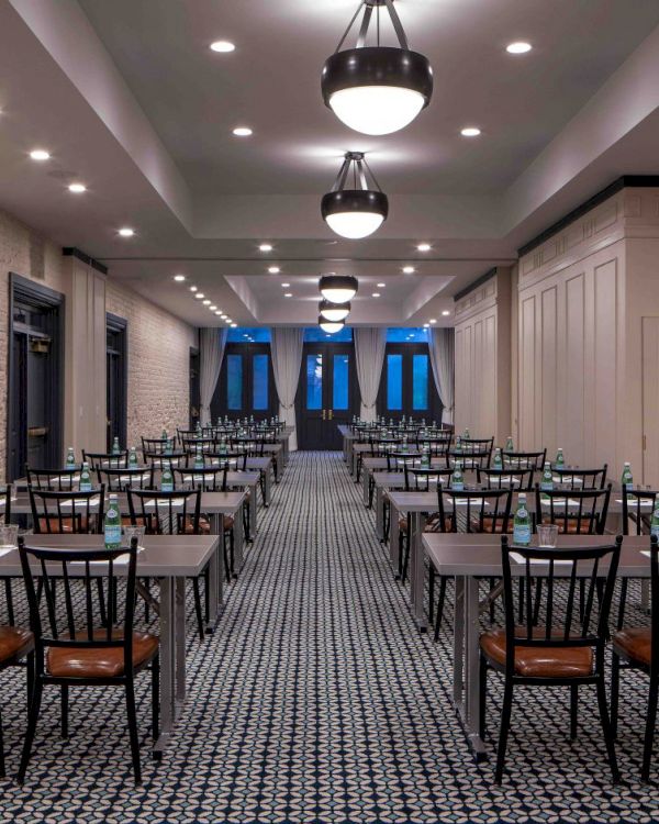 A long, neatly arranged conference room with rows of black chairs and small tables, pendant lights, brick walls, and blue-lit windows at the far end.