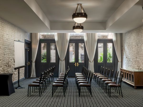 A conference or event room with rows of chairs facing a podium, brick walls, and large windows with draped curtains, ready for a meeting or presentation.