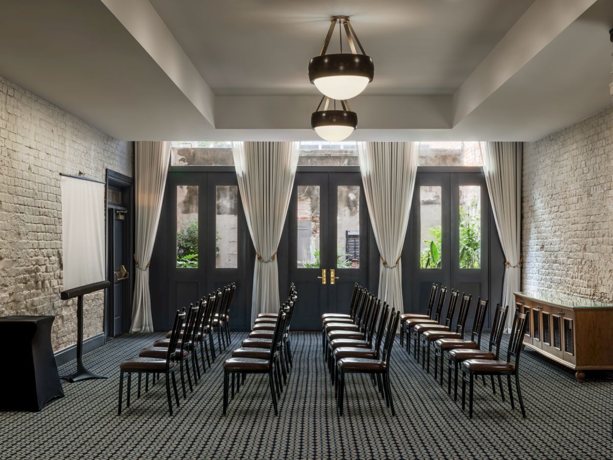 A bright room set for a formal event with rows of black-and-white striped chairs, brick walls, and tall windows with curtains.