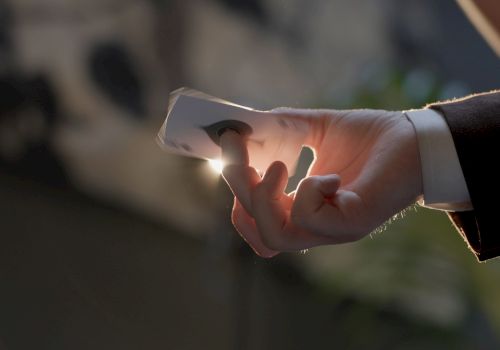 A hand holding a lit cigarette or joint, with a faint glow at the tip, in a suit sleeve, against a blurred background. End.