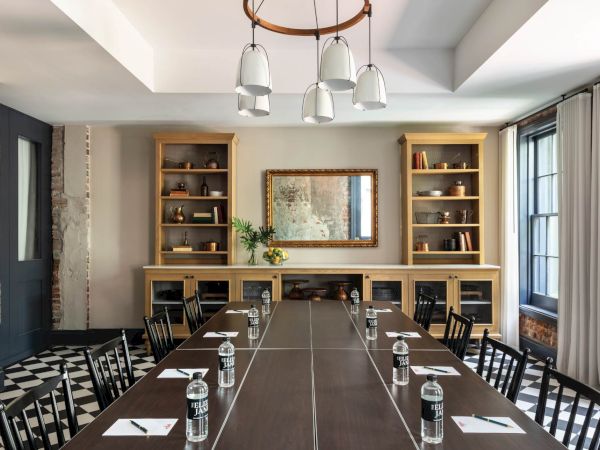 A modern conference room with a long table, black chairs, glassware, notebooks, and a built-in shelving unit with a framed mirror at the far end.