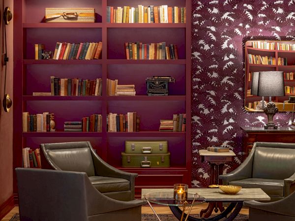 A cozy reading nook with purple shelves, two leather chairs, a glass coffee table, and warm lighting in a stylish, book-filled room.