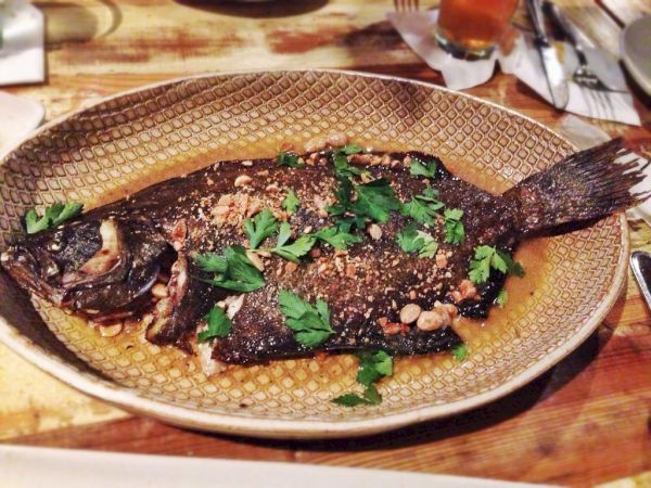 A whole roasted fish topped with chopped parsley on a decorative plate, garnished with herbs and spices.