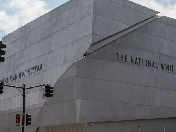 A building with signage reading &ldquo;The National WWII Museum&rdquo; on a modern concrete exterior, under a partly cloudy sky.