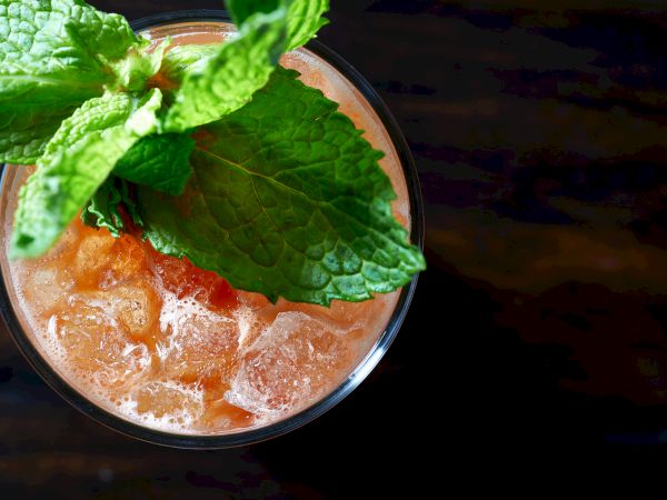 A glass with a fizzy drink and ice, topped with fresh mint leaves against a dark wooden surface.