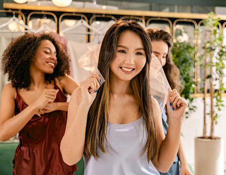 A group of friends at a salon, smiling and wearing face shields, as one woman sits in front ready for a makeover.