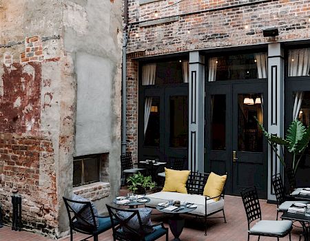 A cozy urban courtyard cafe with exposed brick walls, black-framed doors, and neatly arranged tables and chairs outdoors.