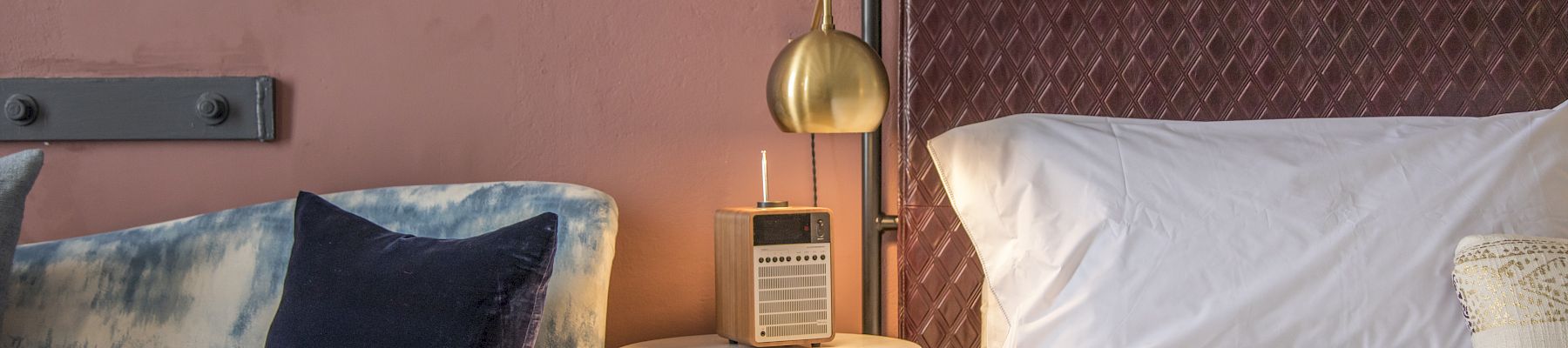 A stylish hotel room corner with a bed, nightstand, brass bedside lamp, and a blue sofa with cushions, neat and modern.