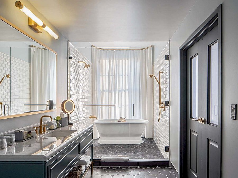 A vintage-style bathroom with two sinks and a freestanding tub by a window, white hex tile walls, brass fixtures, and a dark vanity cabinet.