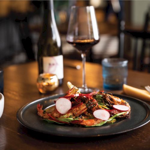 A plated steak with sides and a beer bottle on a wooden table, lit warmly in a cozy dining setting.