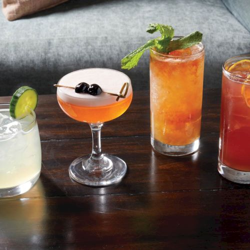A row of colorful cocktails and glassware on a bar counter, with varied hues and garnishes.
