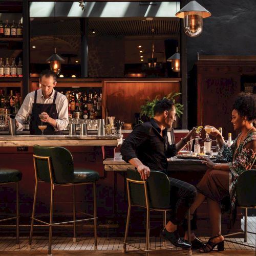 A cozy bar scene with people enjoying drinks around a wooden counter, warm lighting, and a musician performing in the background.