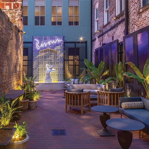 A cozy, narrow alley lined with colorful storefronts, warm lights, and potted plants, leading to a quaint, inviting courtyard at dusk.