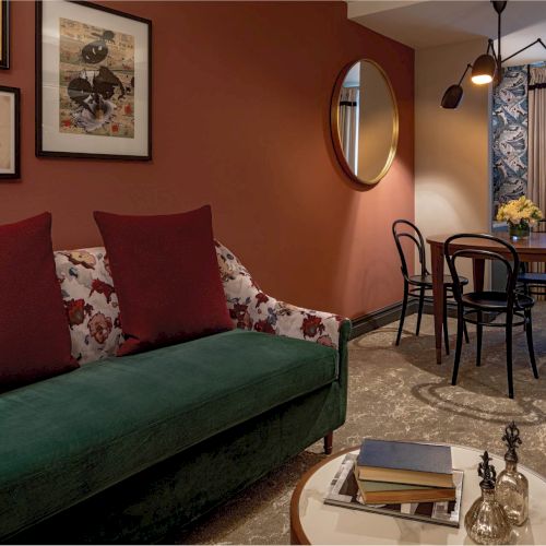 A cozy living room with a red sofa, wood accents, warm lighting, and a small dining area in the background.