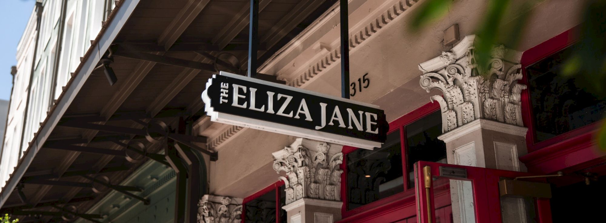 A storefront sign reading &ldquo;The Eliza Jane&rdquo; hangs under a covered sidewalk, with ornate architectural details and red-framed windows.