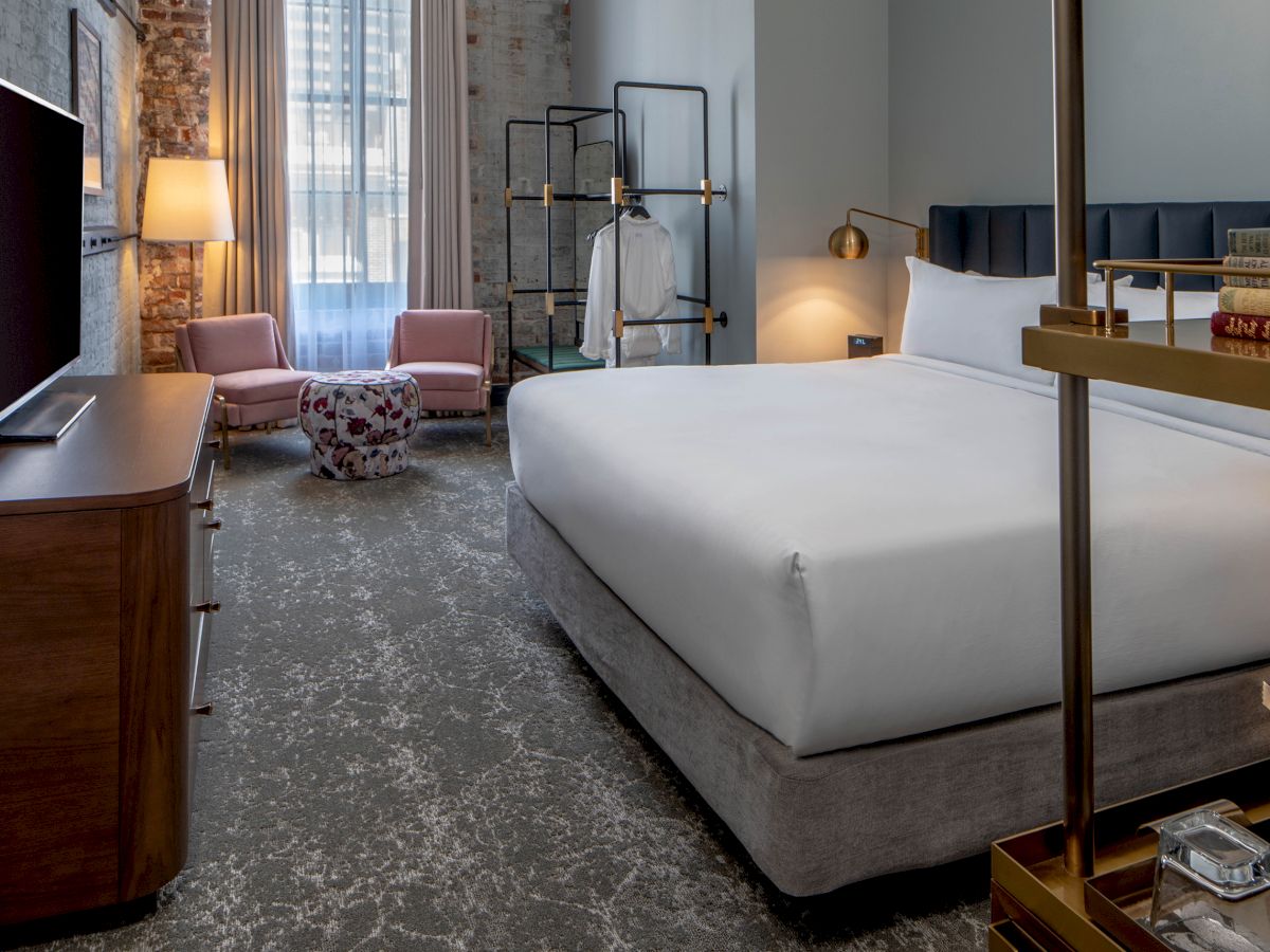 A stylish hotel room with a large bed, seating area, flat-screen TV, and modern decor; a calm, contemporary retreat.