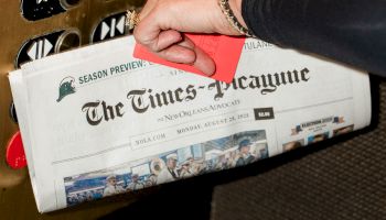 A hand presses an elevator button panel while a newspaper titled &ldquo;The Times-Picayune&rdquo; sits in a hanging mailbox or chute below.