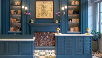 A stylish blue-fronted library reception with built-in shelves, a central fire area, and patterned tiled floor.
