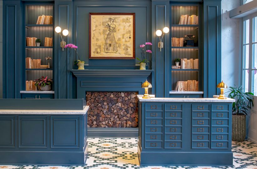 A stylish blue-fronted library reception with built-in shelves, a central fire area, and patterned tiled floor.