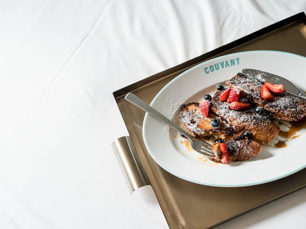 A plate with sliced strawberries and what looks like powdered sugar on a pastry, served on a white dish labeled "COVANT" on a tray.