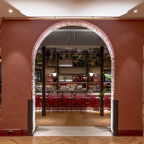 A stylish restaurant entrance with a red arched doorway, warm lighting, and a glimpse of a bar and seating area beyond.